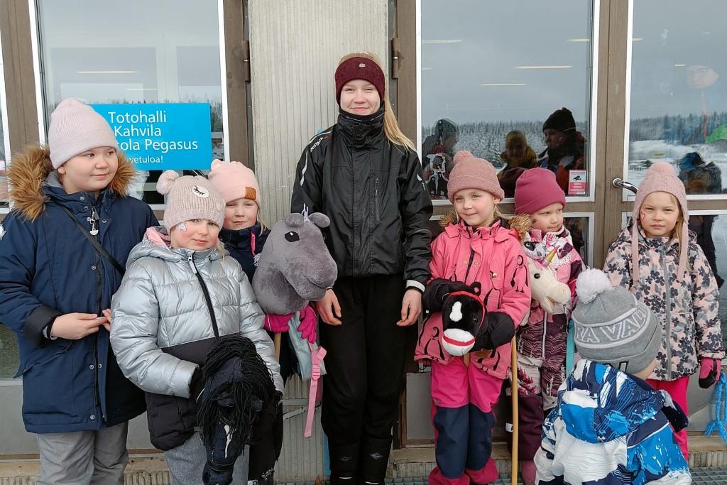 Nuoria ponikerholaisia ohjaajansa ympärillä keppihevoset käsissään.