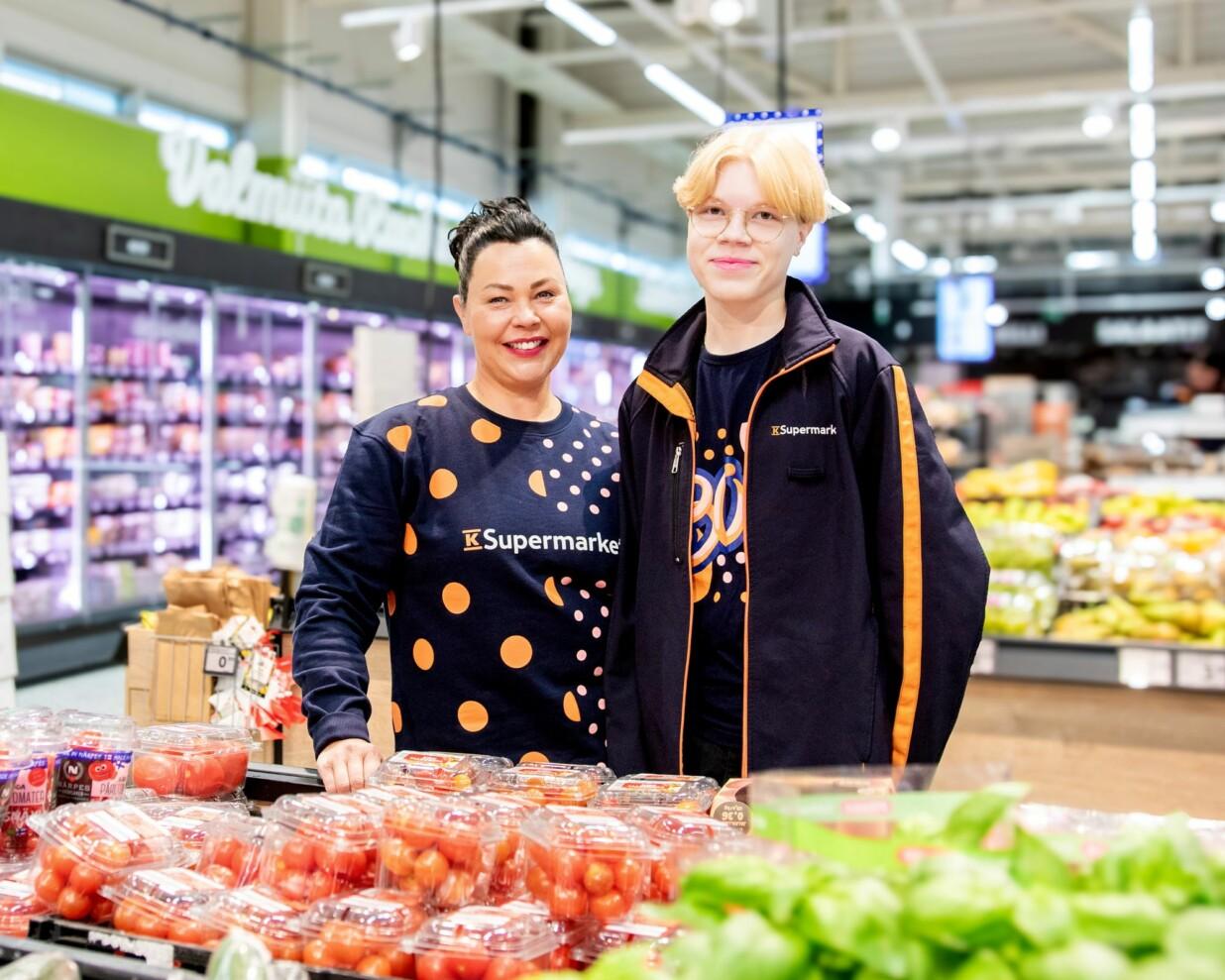 Kauppias ja yhdeksäsluokkalainen kesätyöntekijä poseeraavat kaupassa vihannesosastolla.