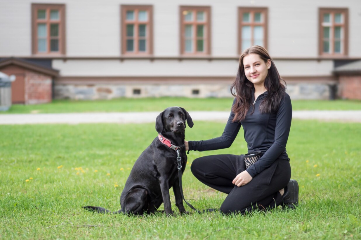 Tyttö silittää mustaa koiraa ulkona.