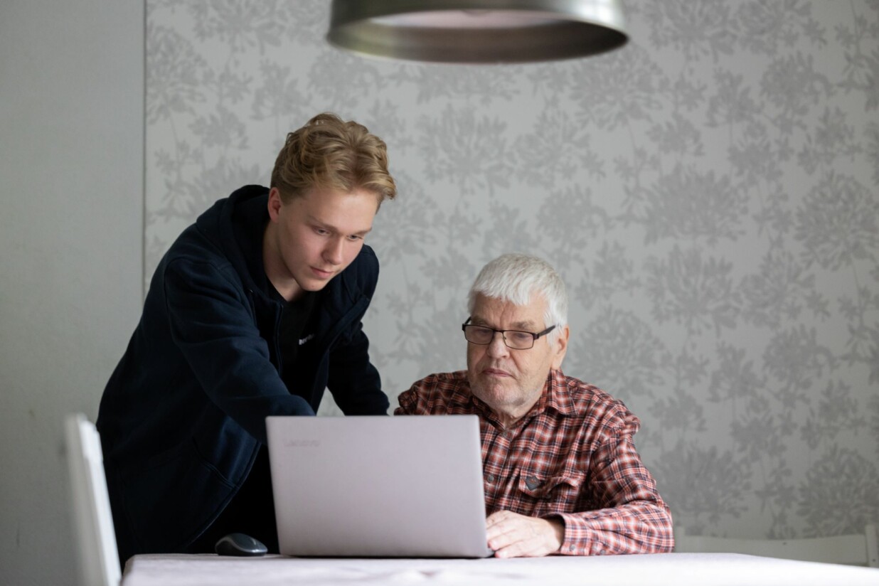 Poika ohjeistaa iäkästä miestä tietokoneen käytössä.