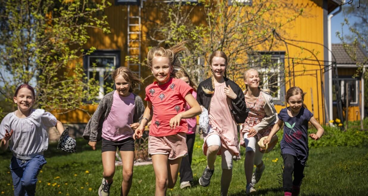 Joukko kerholaisia juoksee iloisena kesäisessä maisemassa.