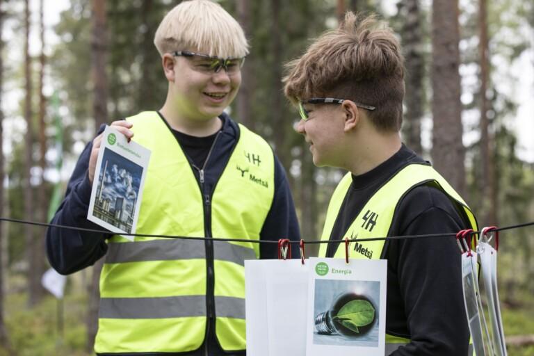 Kaksi poikaa katsovat metsäisessä ympäristössä kuvia, joissa esitellään hiilenkiertoa luonnossa.
