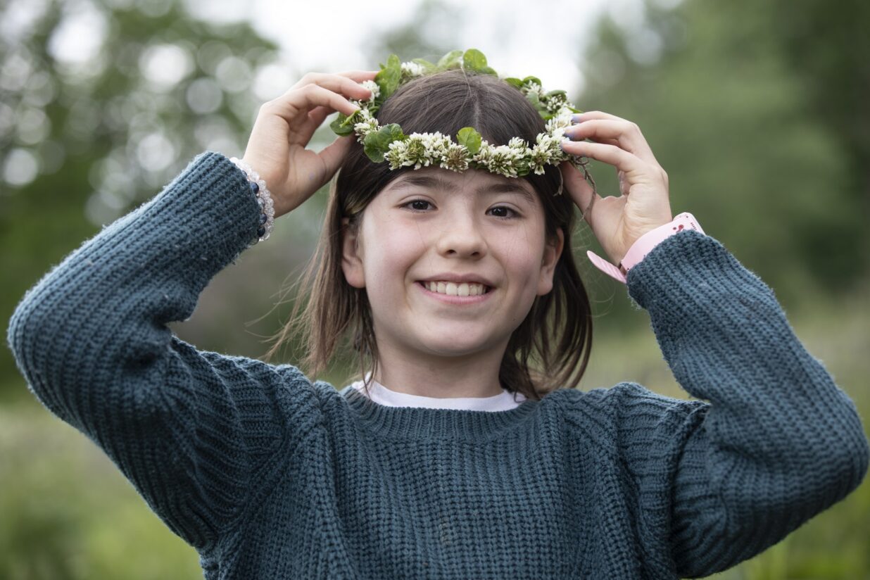 Tyttö hymyilee ja asettelee päähänsä kukkaseppelettä.