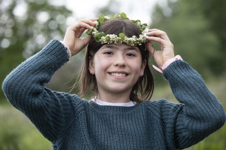 Tyttö hymyilee ja asettelee päähänsä kukkaseppelettä.